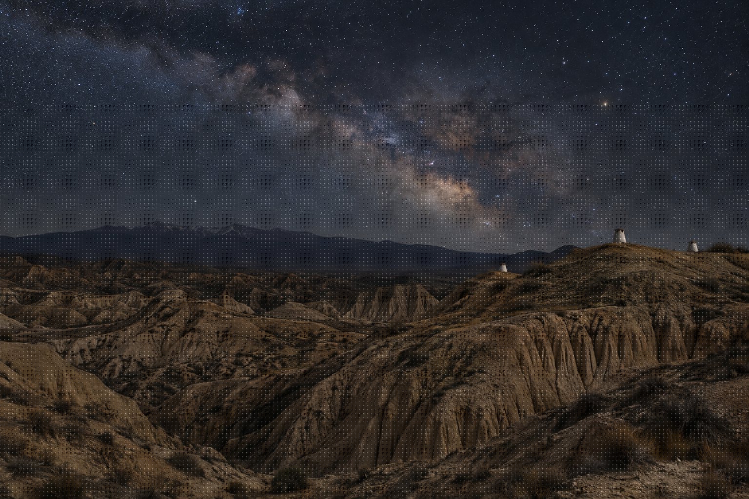 Cielo estrellado sobre las cárcavas de Guadix de noche, con chimeneas blancas de casas cueva apenas iluminadas y sin ninguna luz artificial