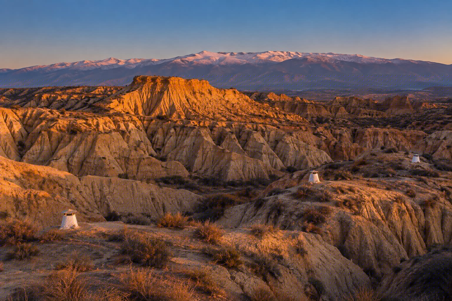 Cárcavas de arcilla del Geoparque de Granada al atardecer, con chimeneas blancas y Sierra Nevada al fondo