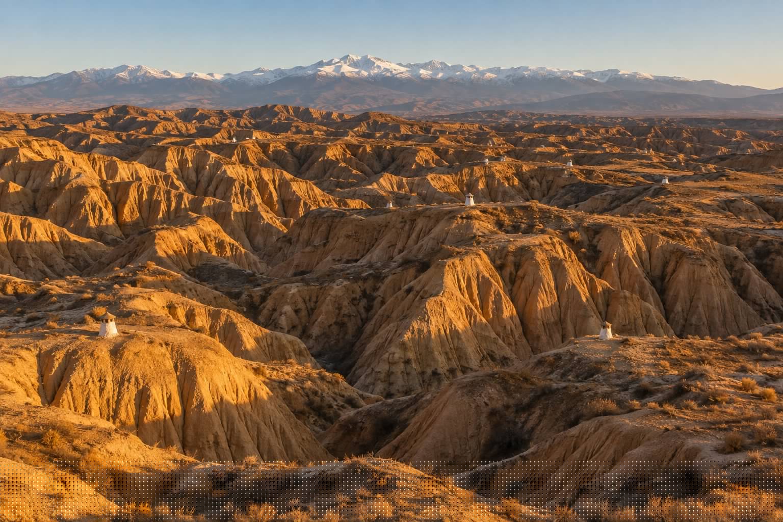 Vista aerea de los barrancos de arcilla ocre de Guadix con chimeneas de casas cueva asomando entre el terreno y Sierra Nevada al fondo (imagen ilustrativa)
