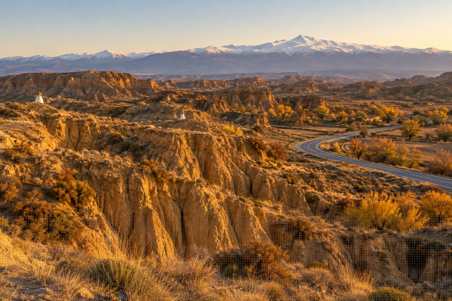 Paisaje del altiplano de Guadix con cárcavas ocres, chimeneas de casas cueva asomando y Sierra Nevada al fondo (imagen ilustrativa)
