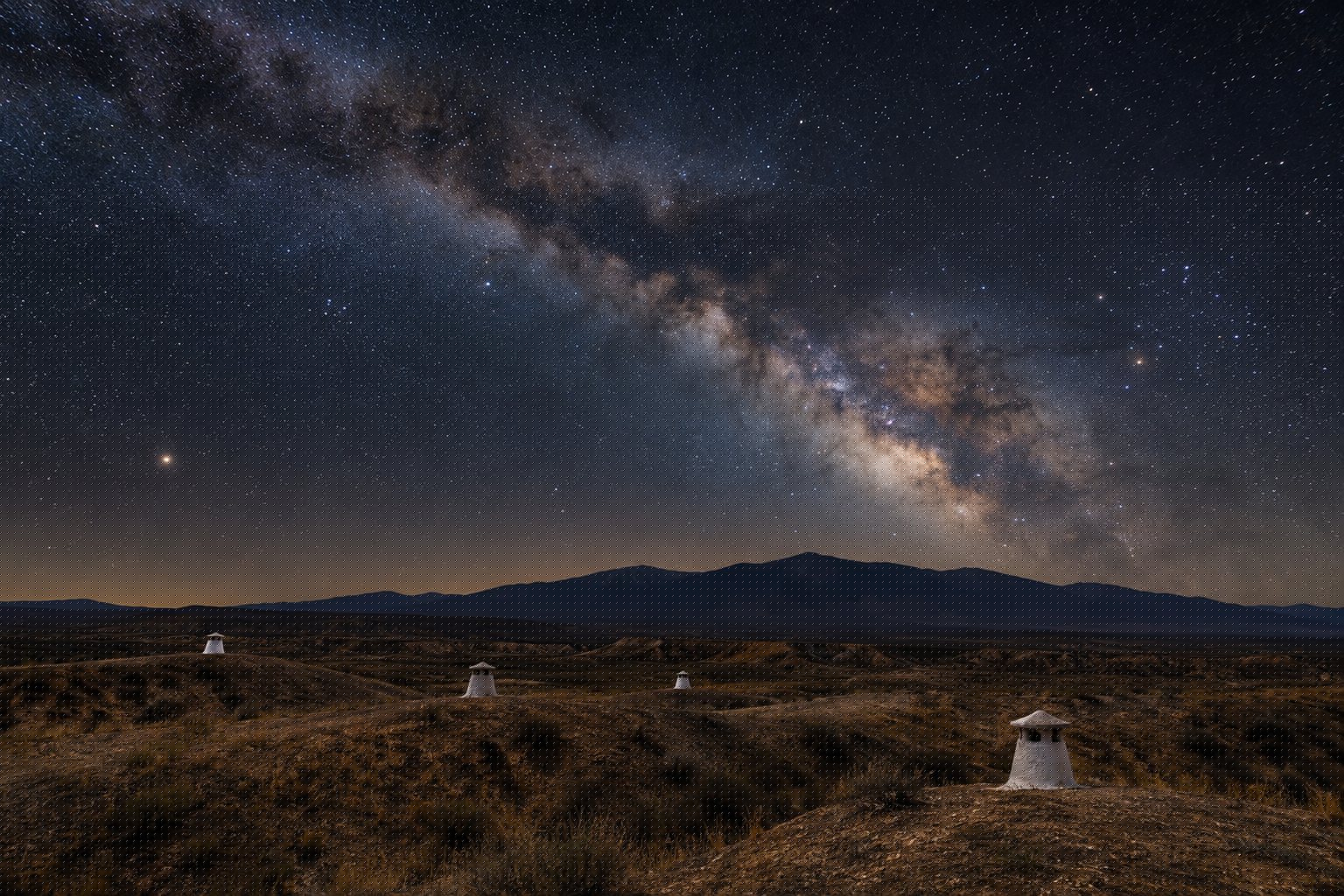 Vía Láctea sobre el altiplano de Guadix con chimeneas blancas de casas cueva asomando del terreno y la silueta de Sierra Nevada al fondo (imagen ilustrativa)