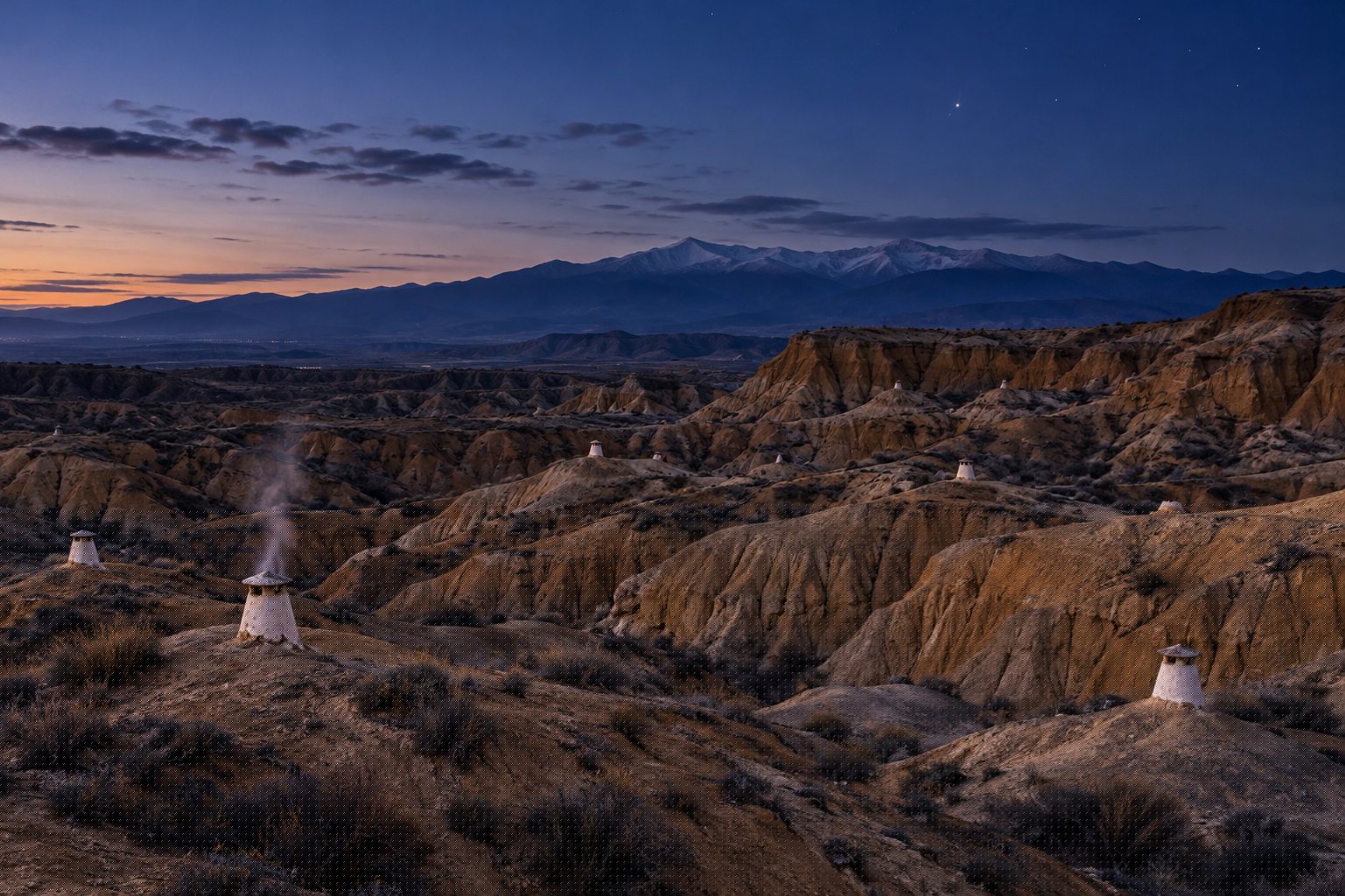 Escapada rural a Guadix: el órgano de Aldeire y el silencio de la cueva 3 Chimeneas blancas de casas cueva asomando entre las cárcavas de Guadix al anochecer, con Sierra Nevada al fondo